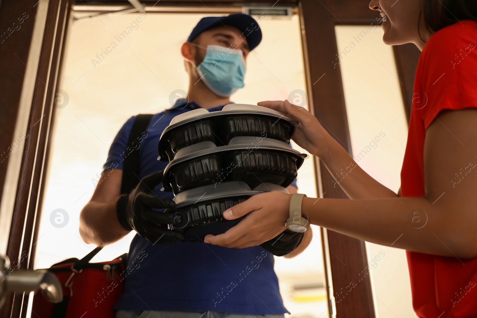 Photo of Courier in protective mask and gloves giving order to woman at entrance. Restaurant delivery service during coronavirus quarantine