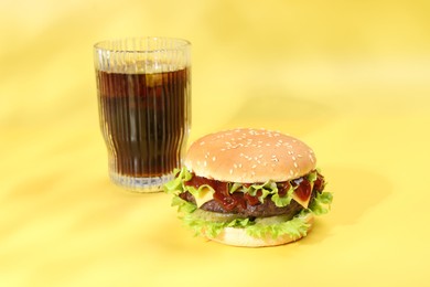 Photo of Burger with delicious patty and soda drink on yellow background