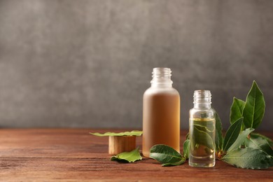 Bottles of bay essential oil and fresh leaves on wooden table. Space for text