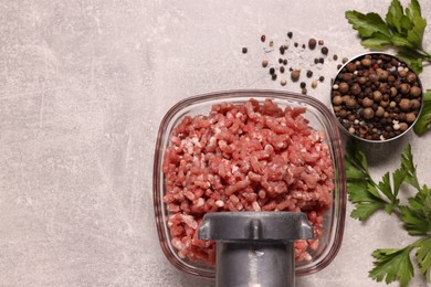Manual meat grinder with beef mince, peppercorns and parsley on light grey table, flat lay. Space for text