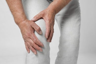 Senior man having knee problems on grey background, closeup