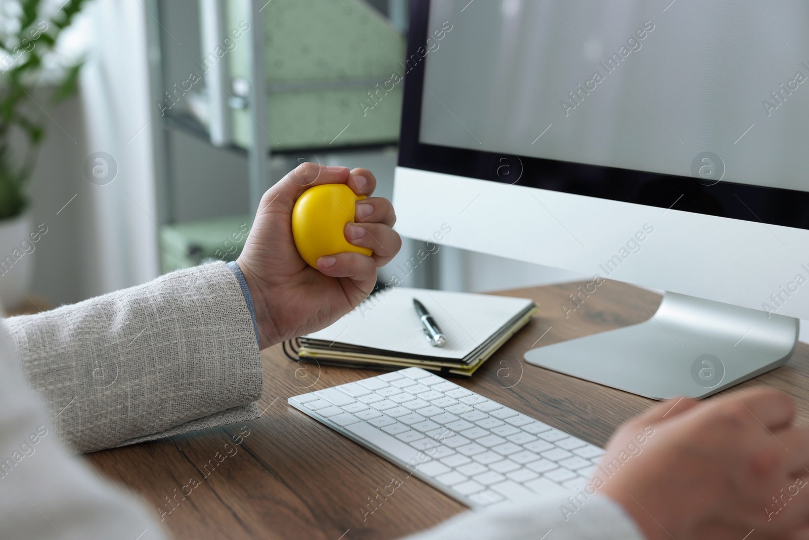 Photo of Man squeezing antistress ball while working with computer in office, closeup