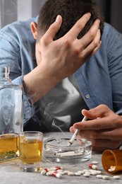 Photo of Alcohol and drug addiction. Man with smoldering cigarettes, whiskey and pills at grey textured table