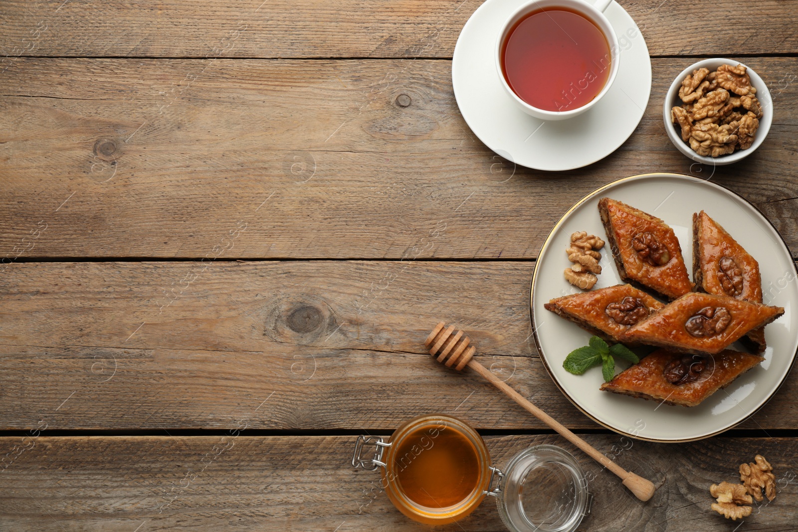 Photo of Delicious honey baklava with walnuts served on wooden table, flat lay. Space for text