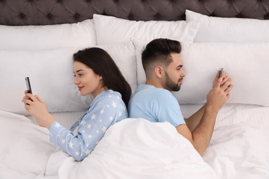Photo of Young couple addicted to smartphones in bed at home, above view