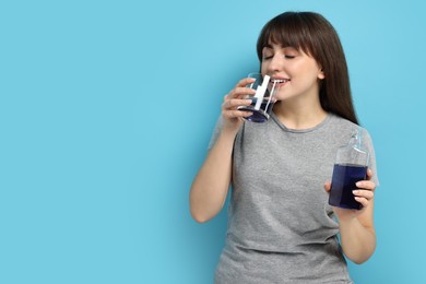 Young woman using mouthwash on light blue background, space for text