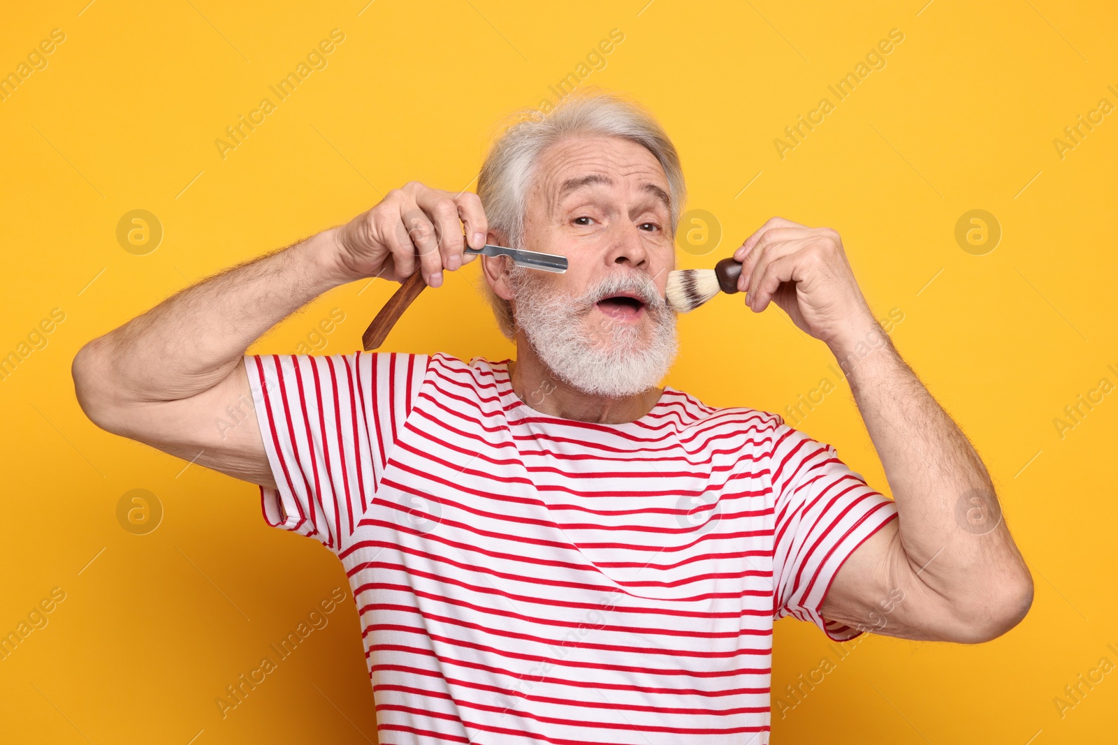 Photo of Senior man with mustache holding blade and brush on orange background