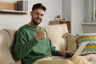 Photo of Handsome man with laptop sitting on sofa at home