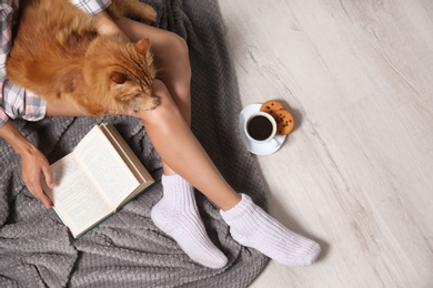 Photo of Woman with cute red cat and book on floor, top view. Space for text