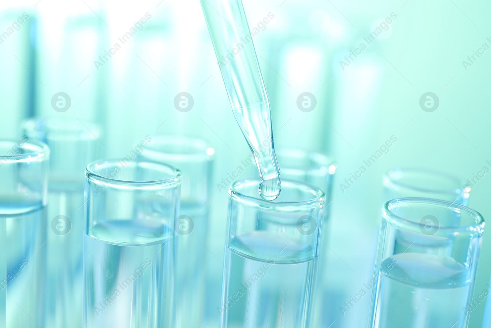 Photo of Dripping liquid from pipette into test tube on turquoise background, closeup