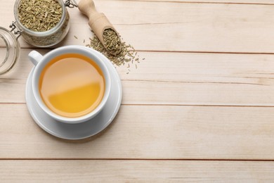 Fennel tea in cup and seeds on light wooden table, flat lay. Space for text