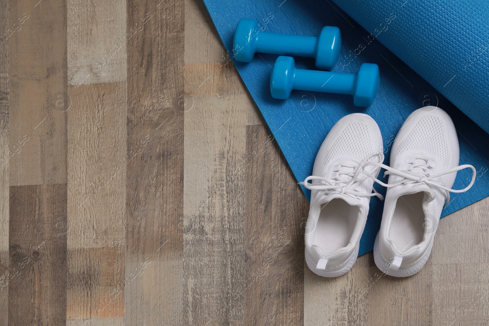 Photo of Dumbbells, sneakers and mat on wooden floor, above view. Space for text