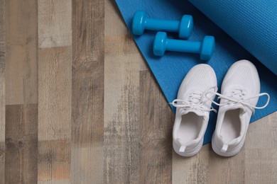 Dumbbells, sneakers and mat on wooden floor, above view. Space for text