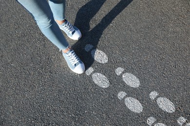 Image of Planning future. Woman walking on drawn marks on road, closeup. White footsteps showing direction of way
