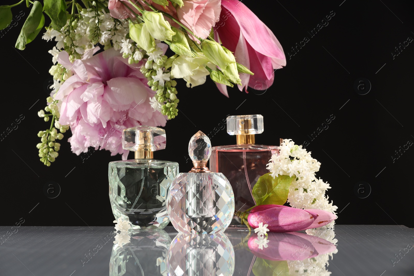 Photo of Luxury perfumes and floral decor on mirror surface against black background