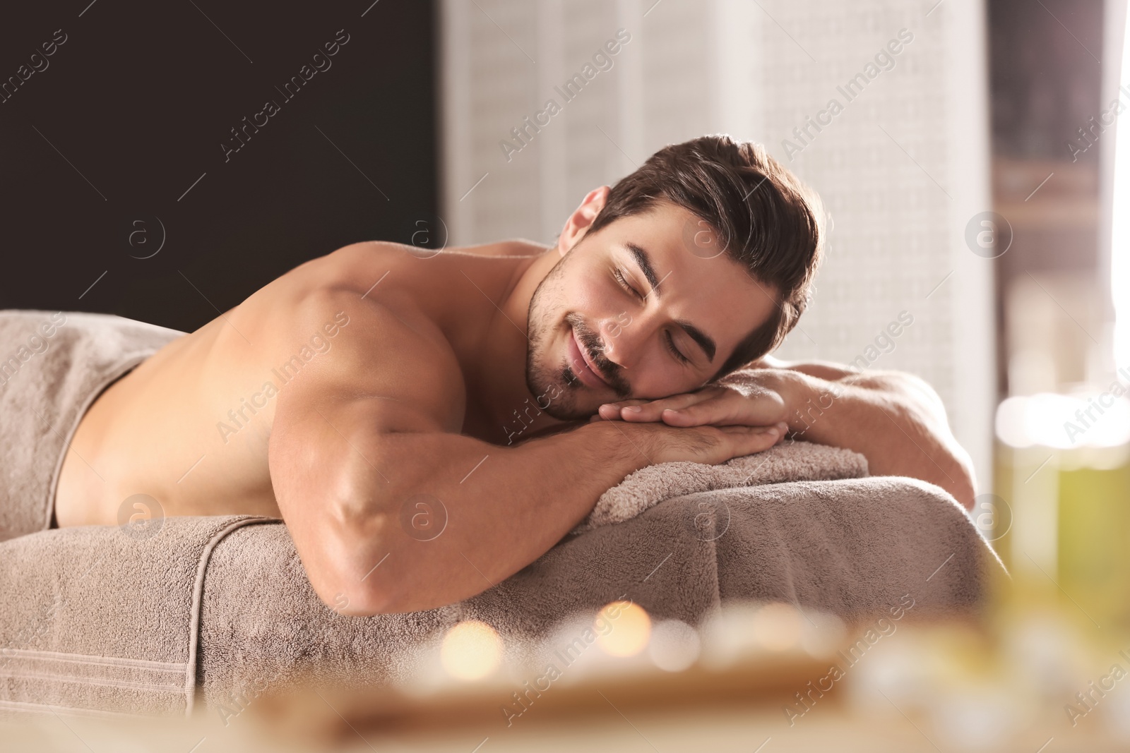 Photo of Handsome young man relaxing on massage table in spa salon