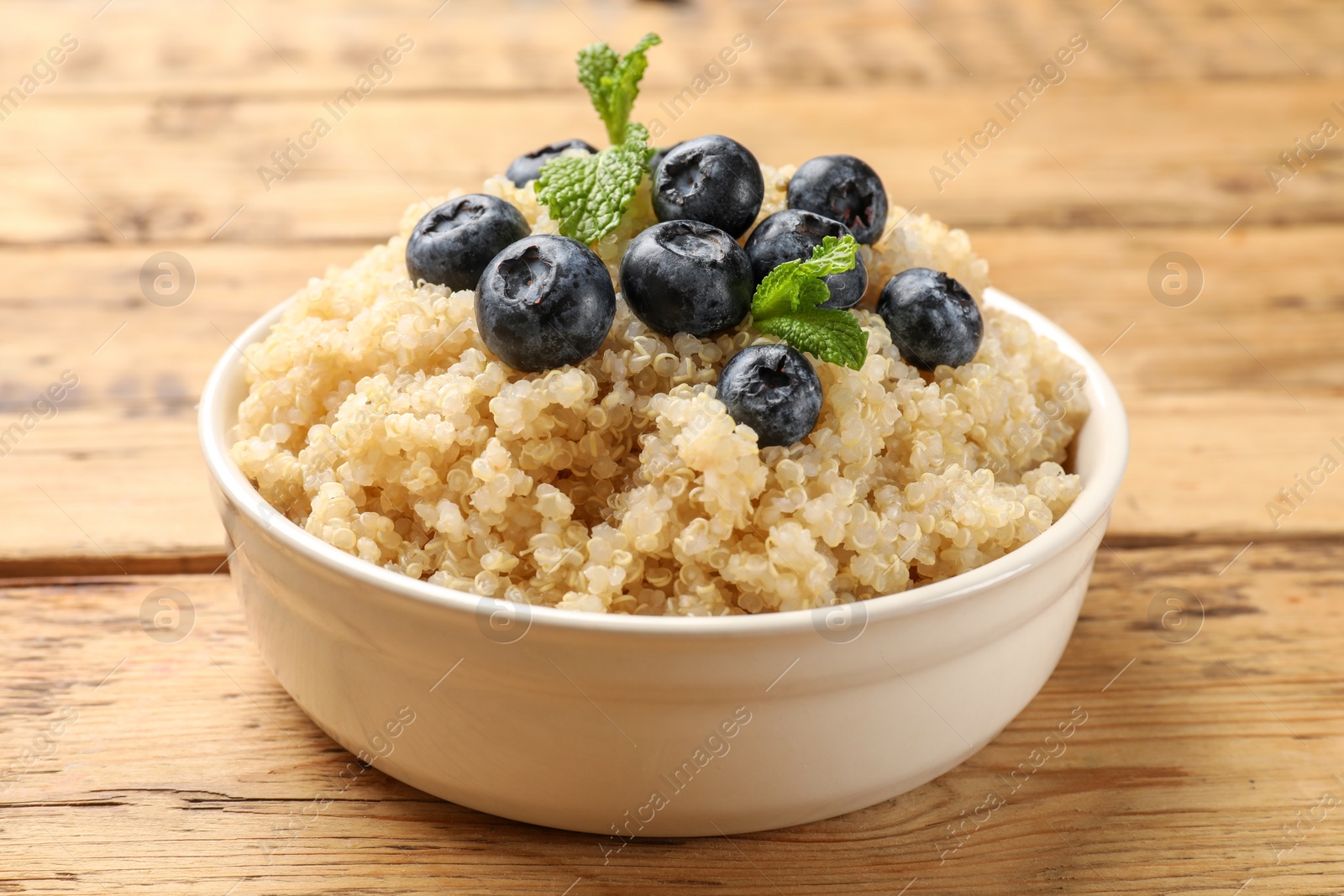 Photo of Tasty quinoa porridge with blueberries and mint in bowl on wooden table, closeup