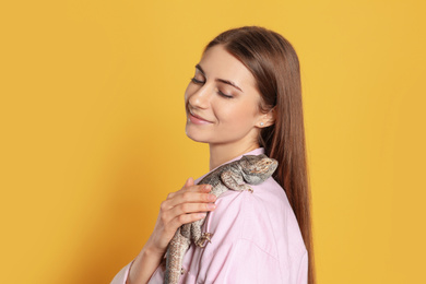 Woman holding bearded lizard on yellow background. Exotic pet