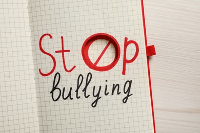 Open notebook with phrase Stop Bullying on white wooden table, top view