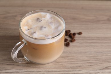 Cup of fresh iced coffee and beans on wooden table, closeup. Space for text