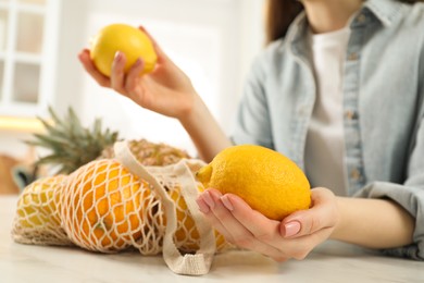 Photo of Woman with lemons and string bag of fresh fruits at light table, closeup