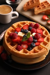 Tasty Belgian waffles with fresh berries, cheese and cup of coffee on black table