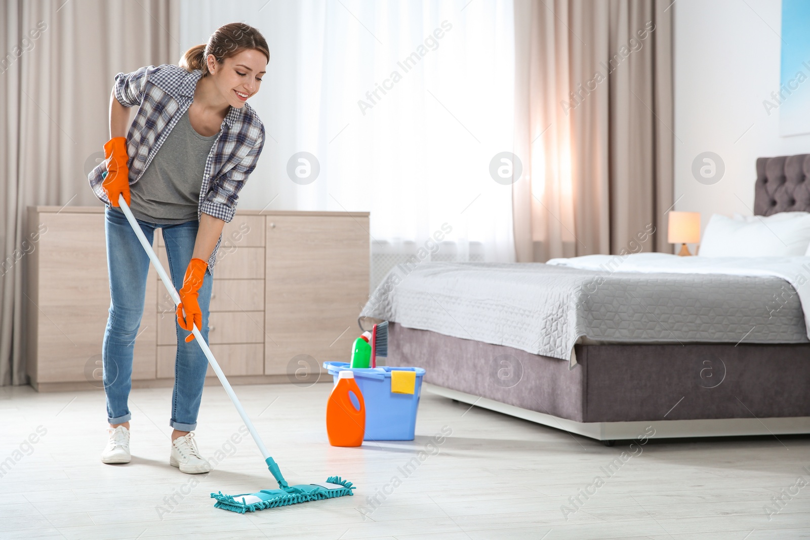 Photo of Young woman washing floor with mop in bedroom, space for text. Cleaning service