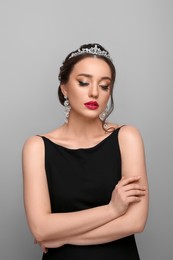 Beautiful young woman wearing luxurious tiara on light grey background