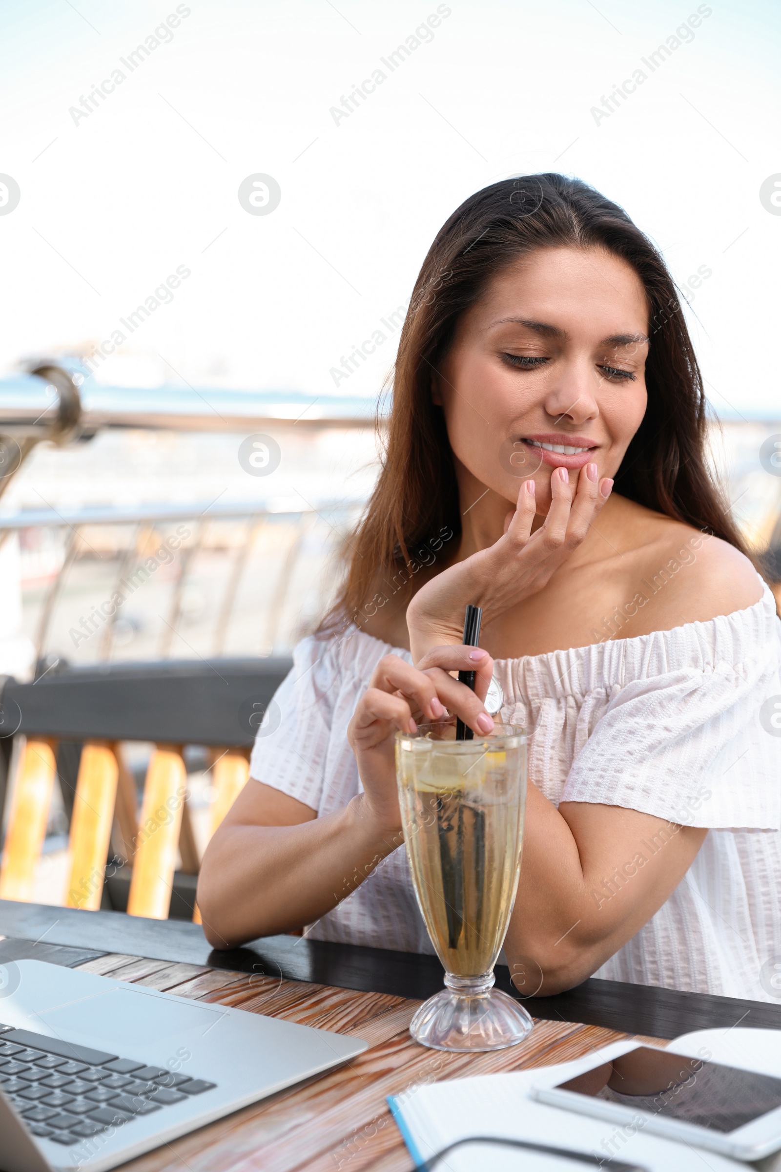 Photo of Beautiful woman with refreshing drink and laptop at outdoor cafe