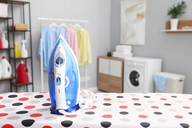 Photo of Clothes iron on ironing board in laundry room, space for text