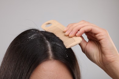 Woman with comb examining her hair and scalp on grey background, closeup. Dandruff problem