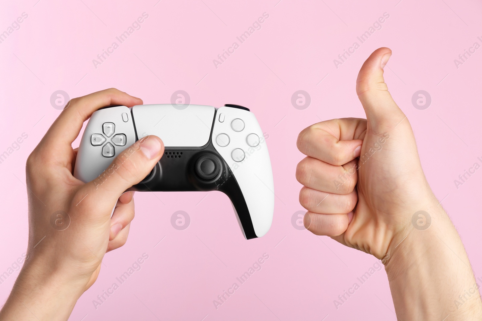 Photo of Man using wireless game controller and showing thumbs up on pink background, closeup