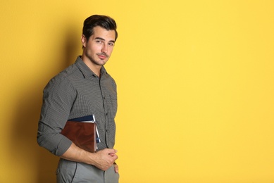 Young male teacher with books on yellow background. Space for text