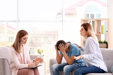Photo of Young female psychologist working with teenage boy and his mother in office