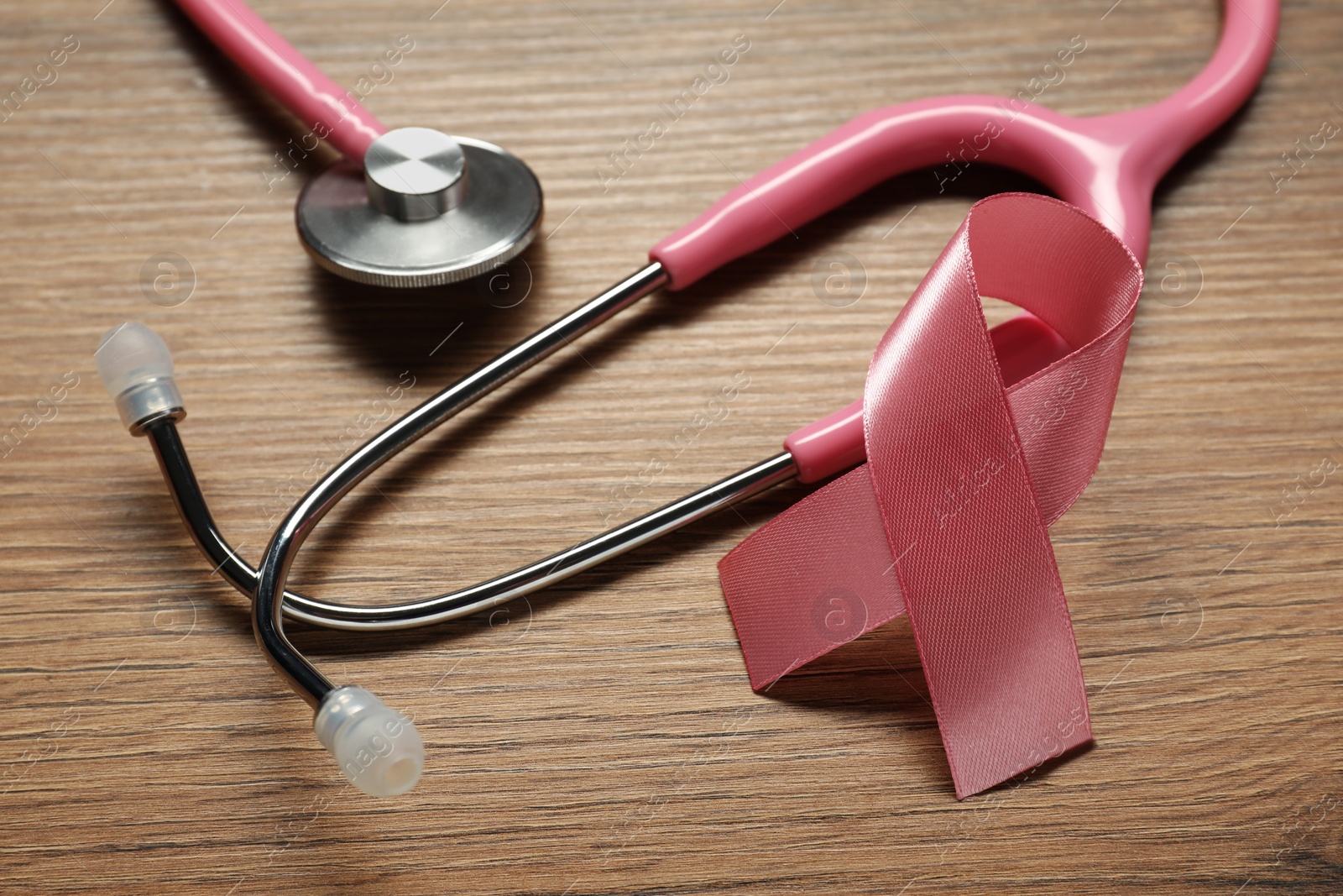 Photo of Pink ribbon and stethoscope on wooden table, closeup. Breast cancer awareness