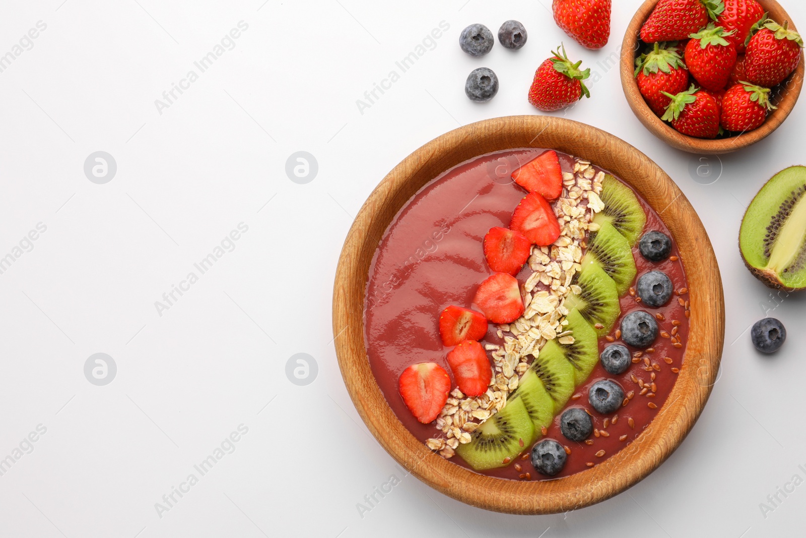 Photo of Bowl of delicious smoothie with fresh blueberries, strawberries, kiwi slices and oatmeal on white background