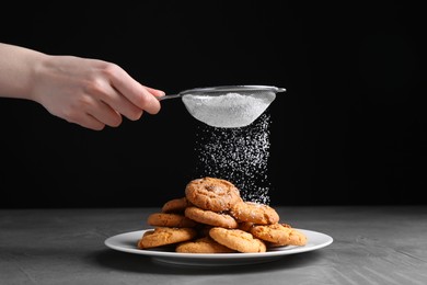 Woman with sieve sprinkling powdered sugar onto cookies at grey textured table, closeup