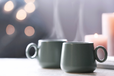 Cups of hot drink on white table against blurred background, space for text