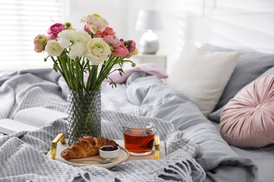 Photo of Bouquet of beautiful ranunculuses, croissant and tea on bed indoors