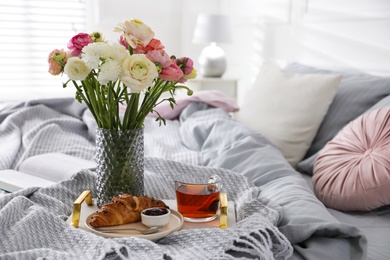 Bouquet of beautiful ranunculuses, croissant and tea on bed indoors