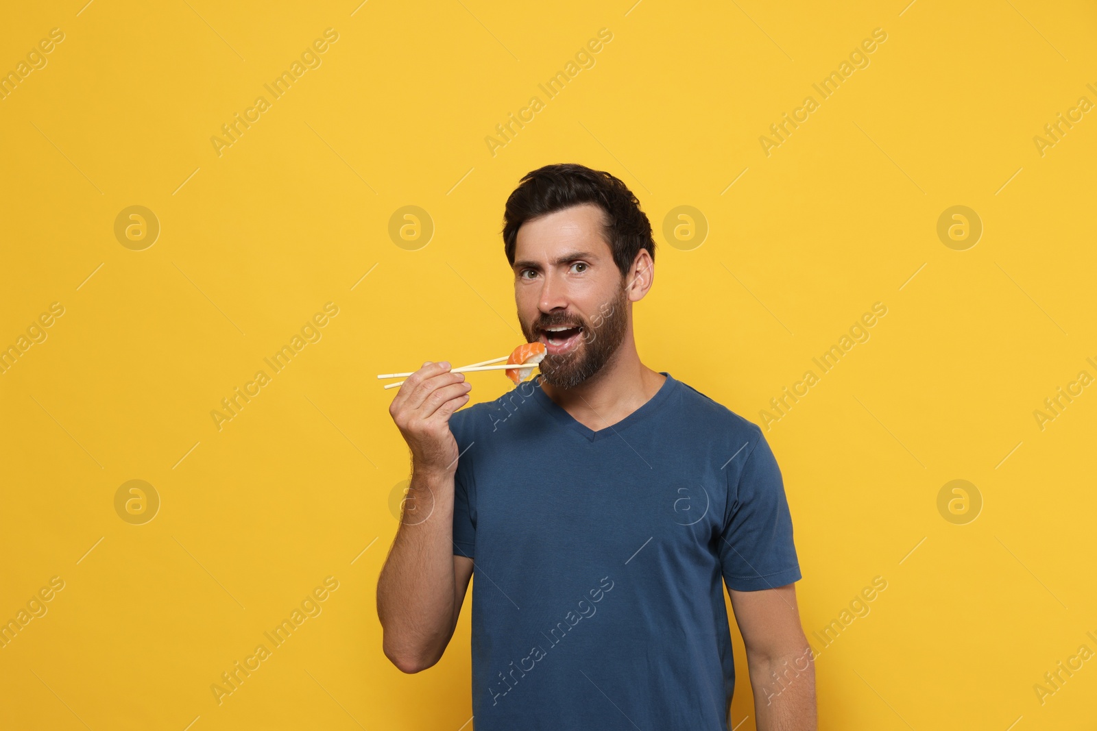 Photo of Handsome man eating sushi with chopsticks on orange background