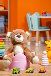 Photo of Teddy bear on pink baby potty and many other toys in room. Toilet training