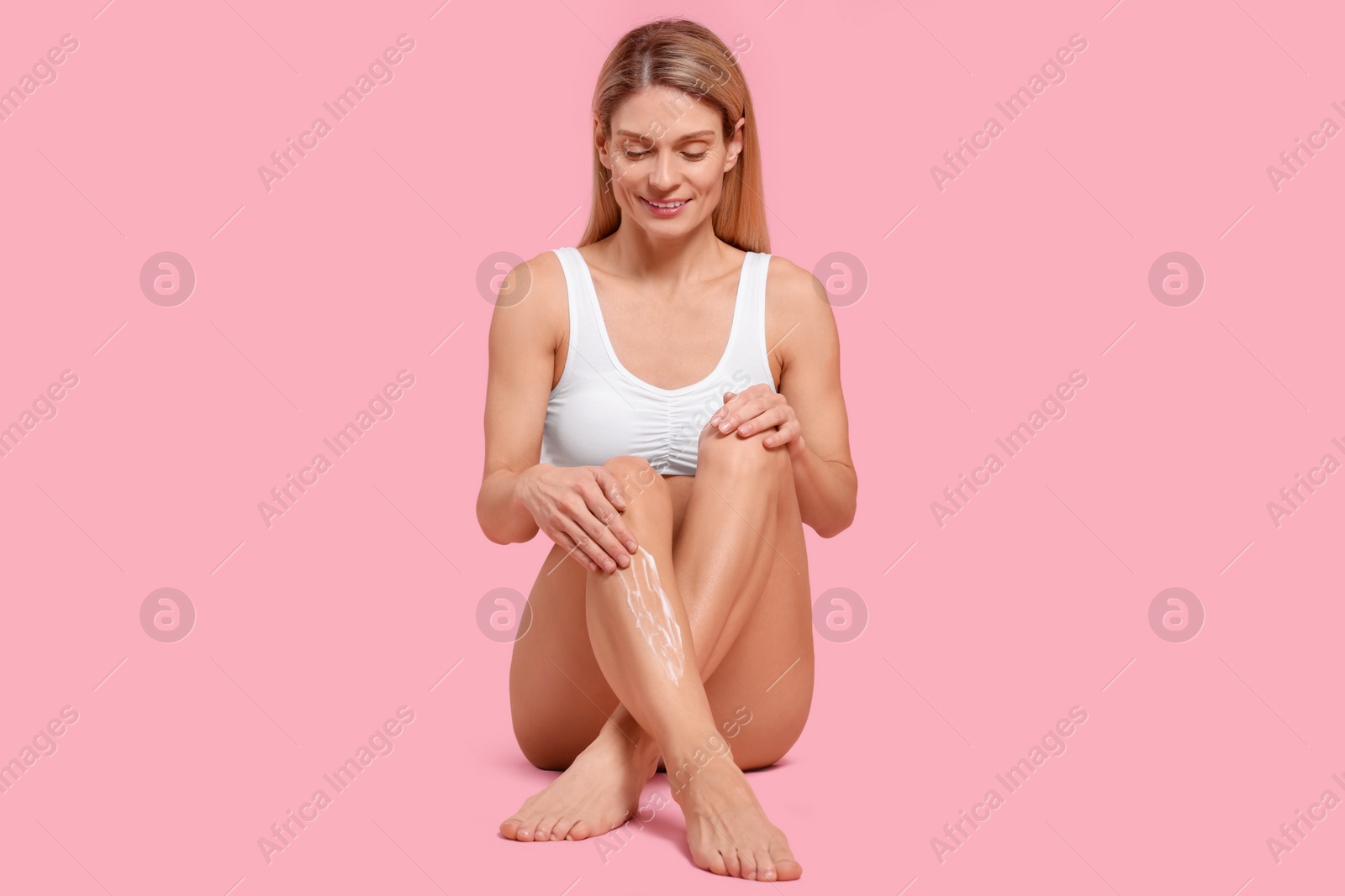 Photo of Woman applying body cream onto her leg against pink background