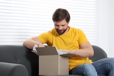 Photo of Happy man opening parcel at home. Internet shopping