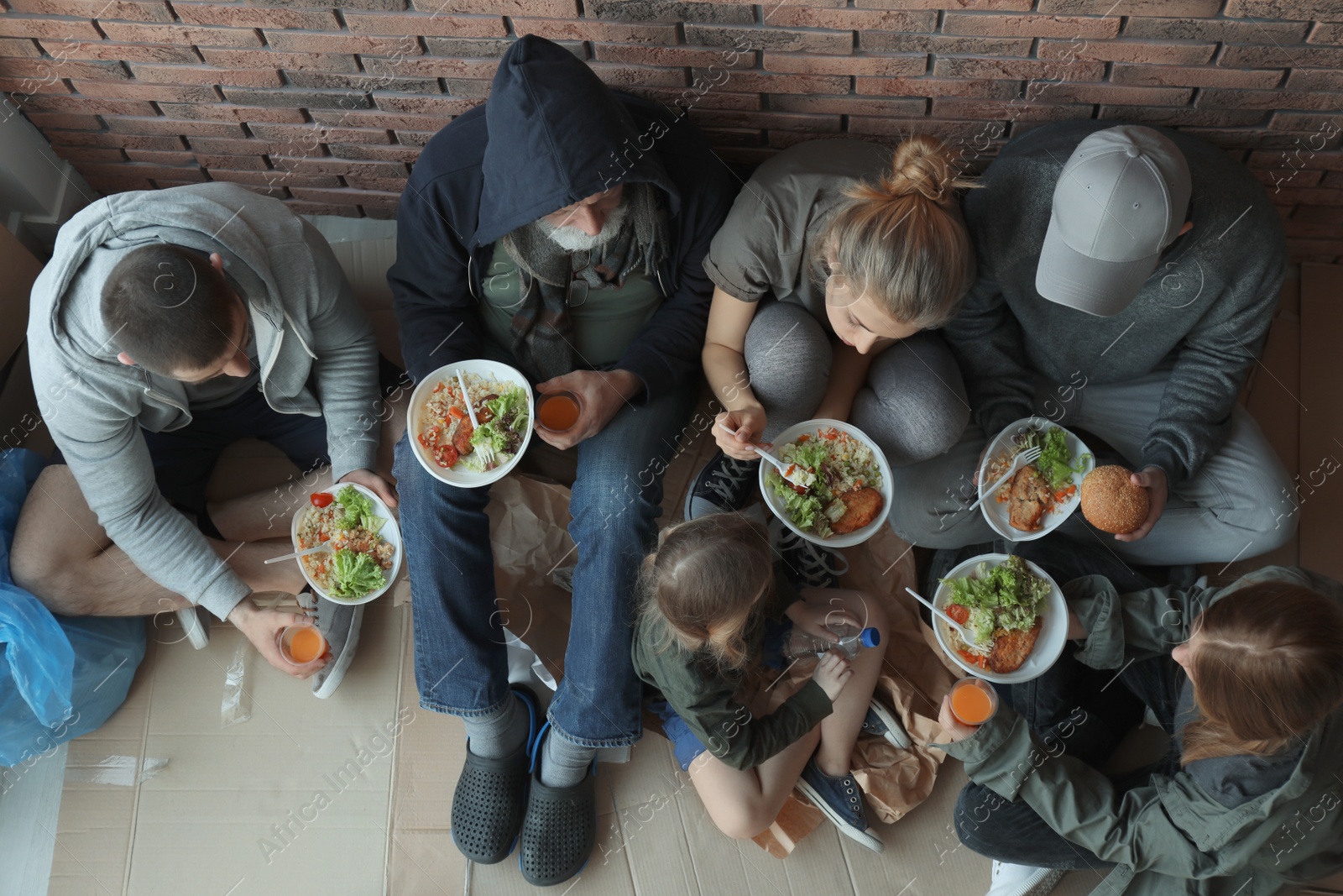 Photo of Poor people with plates of food sitting at wall indoors, view from above