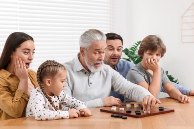 Photo of Emotional family playing checkers at wooden table in room