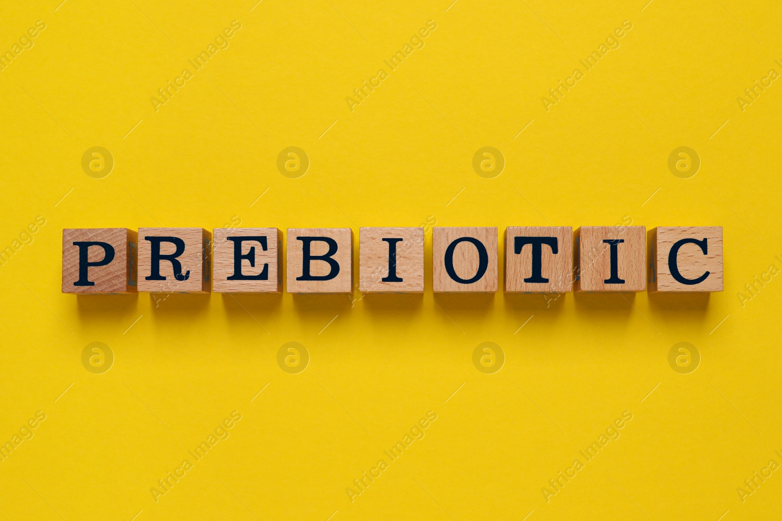 Photo of Wooden cubes with word Prebiotic on yellow background, flat lay