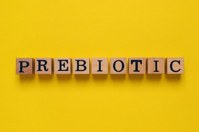 Wooden cubes with word Prebiotic on yellow background, flat lay