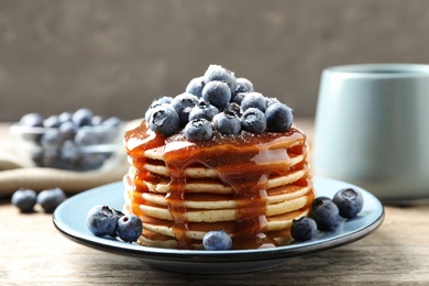 Delicious pancakes with fresh blueberries and syrup on wooden table