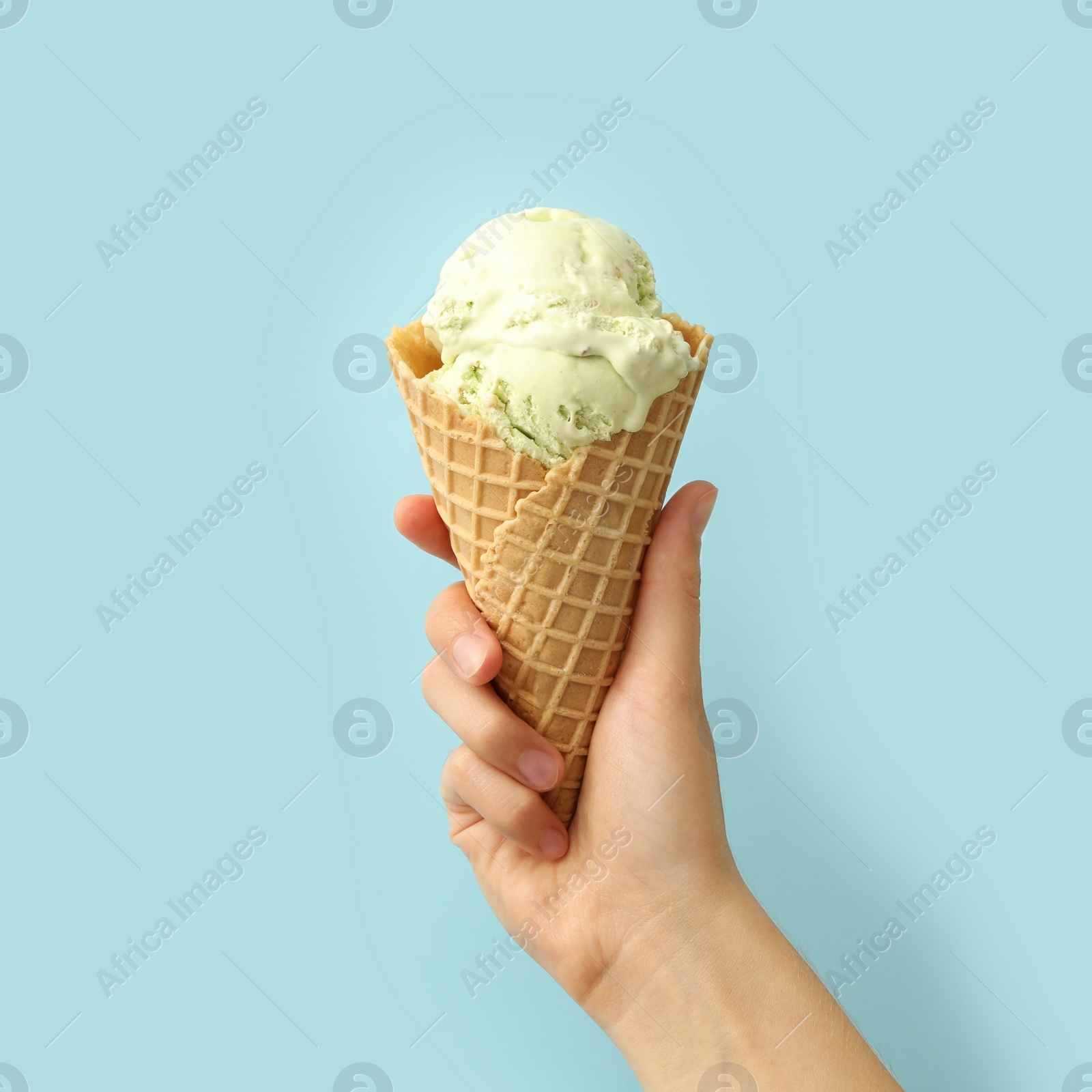 Photo of Woman holding waffle cone with delicious ice cream on light blue background, closeup